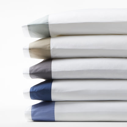 Stack of five wide-band percale pillowcases in seafoam green, taupe, charcoal, navy, and light blue.