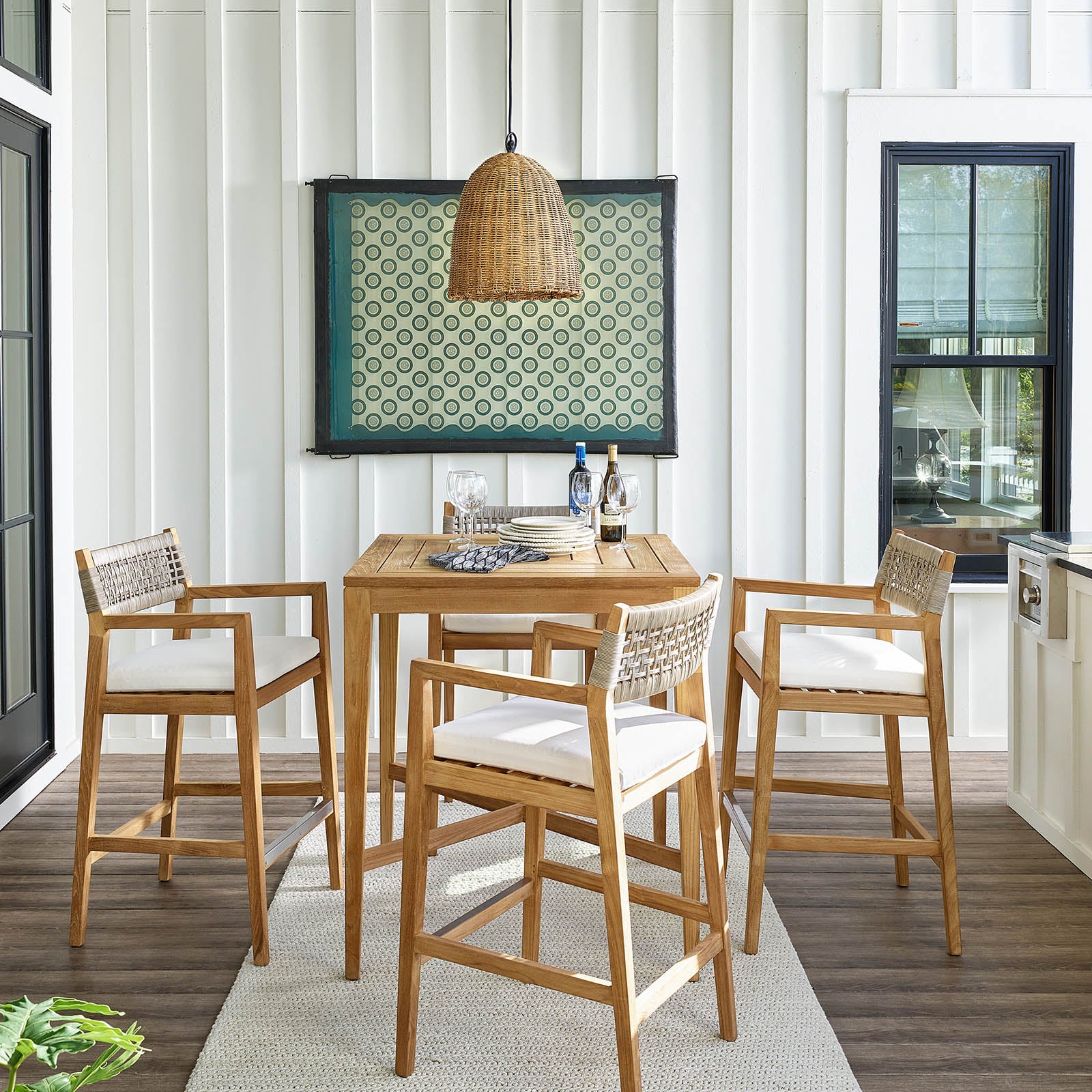 Woven rattan beehive pendant light over a wooden outdoor bar table with four matching stools.