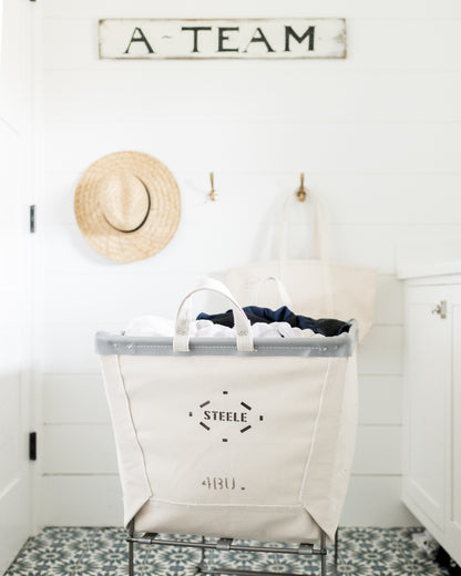 Steele 4-Bushel Canvas Elevated Rolling Laundry Hamper with gray trim and logo, filled with clothes.