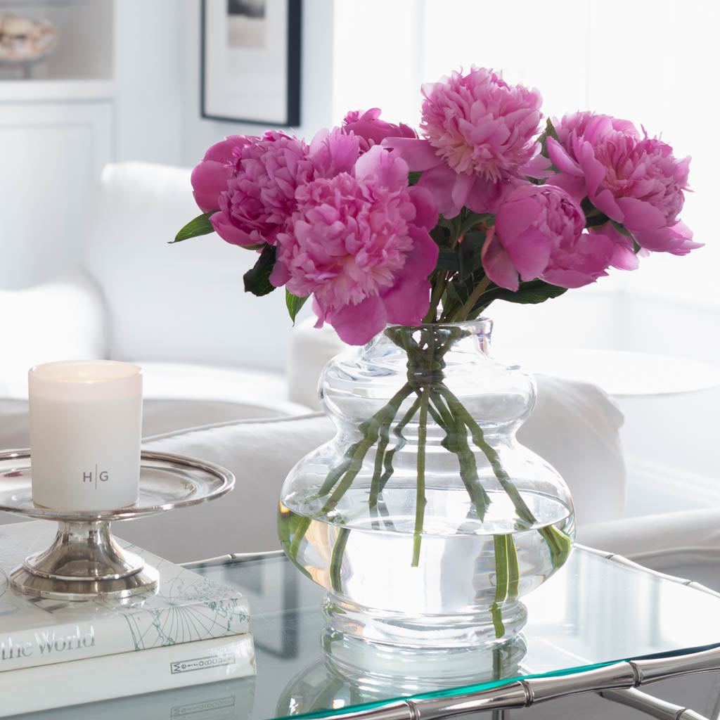 Sylvia Glass Vase, clear mouth-blown glass, 9.5"H, with pink peonies on a glass table.