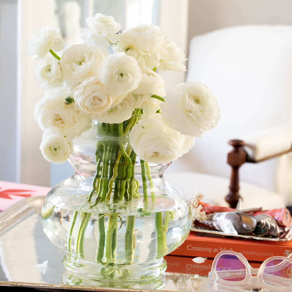 Sylvia Glass Vase, clear mouth-blown glass with white ranunculus, 9.5"H x 9.1"W, on a silver tray.