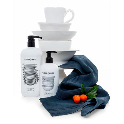 Hudson Grace Tart Kumquat Dish Soap and Hand Lotion, white bottles with black pumps, next to a blue linen towel and kumquats.