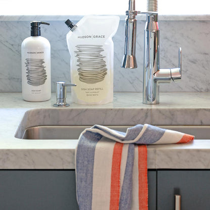 HG Tart Kumquat Dish Soap Refill Pouch and pump bottle on a marble counter with a striped towel.