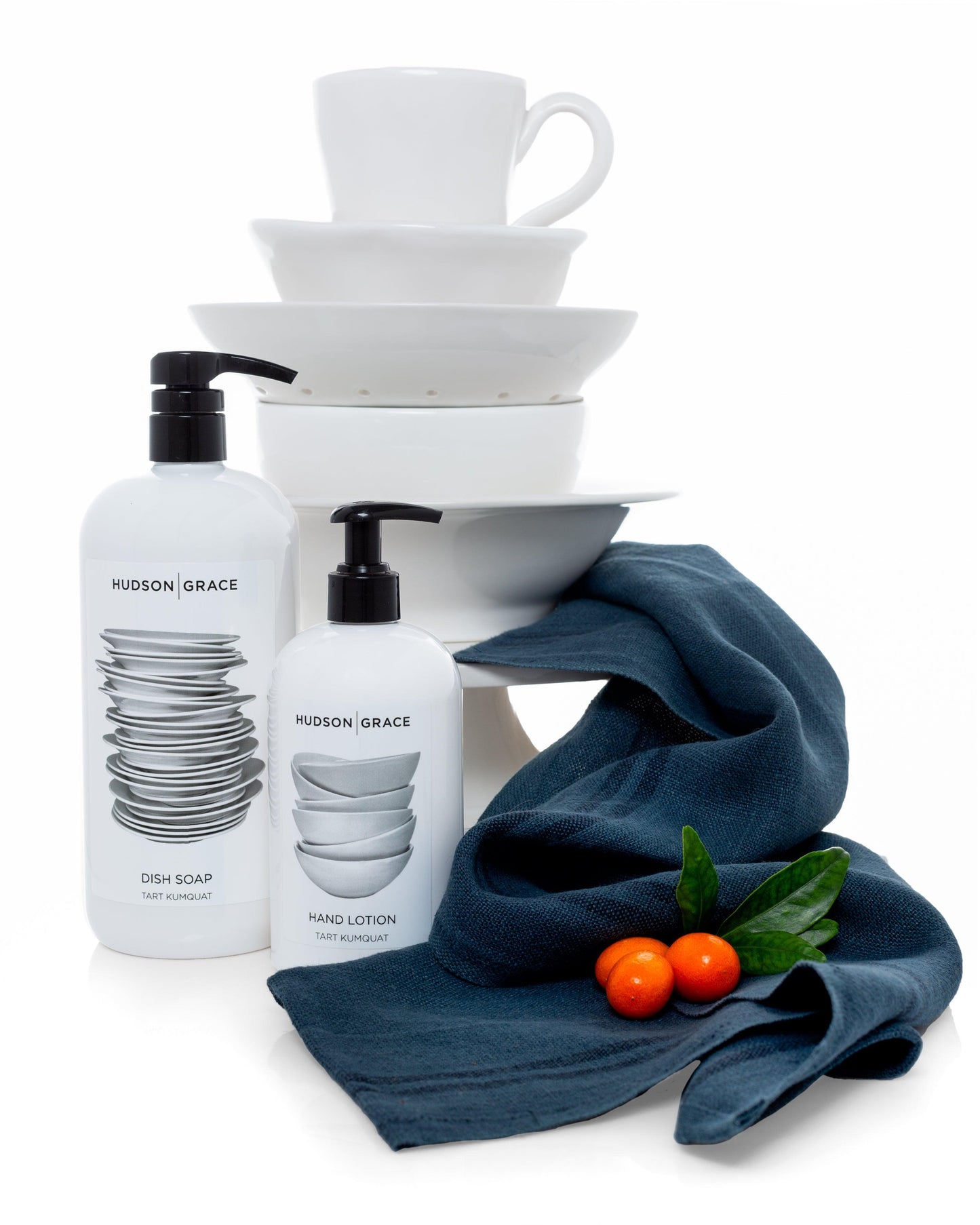 Hudson Grace Tart Kumquat Hand Lotion and Dish Soap, white bottles with black pumps, next to a blue linen towel and kumquats.