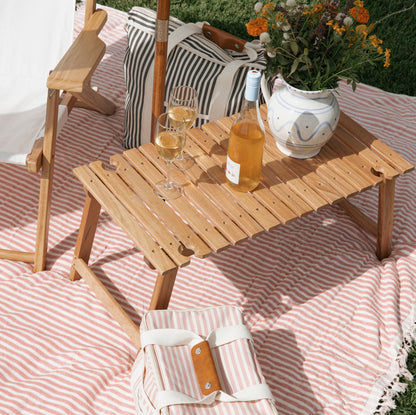 Teak portable outdoor picnic table with folding legs, wine glasses, bottle, and flowers on a striped blanket.