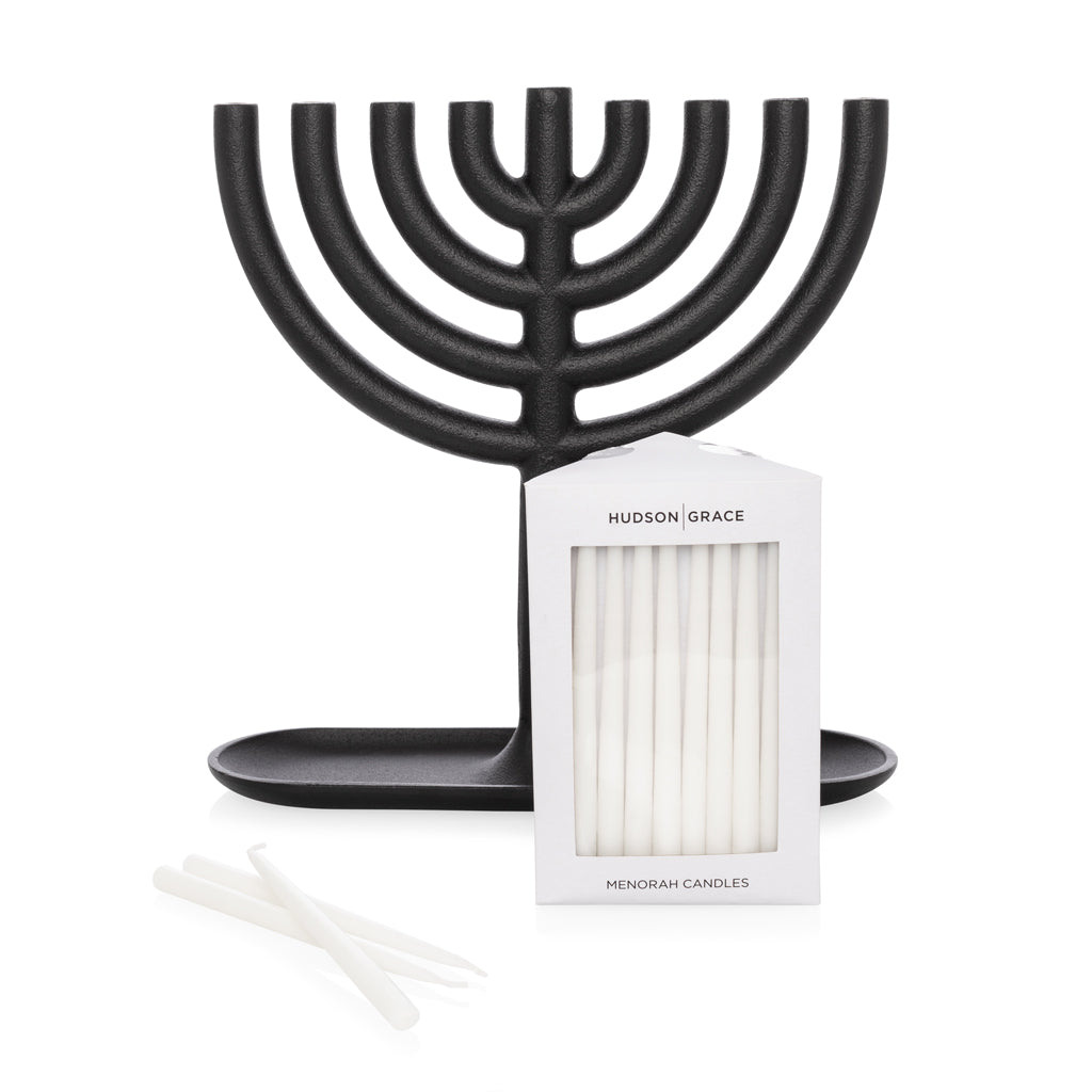 Black cast-iron Menorah with a box of white, delicate taper Hanukkah candles and a few loose candles.