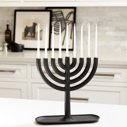 Black cast-iron Menorah with eight white, delicate taper candles on a white kitchen counter.
