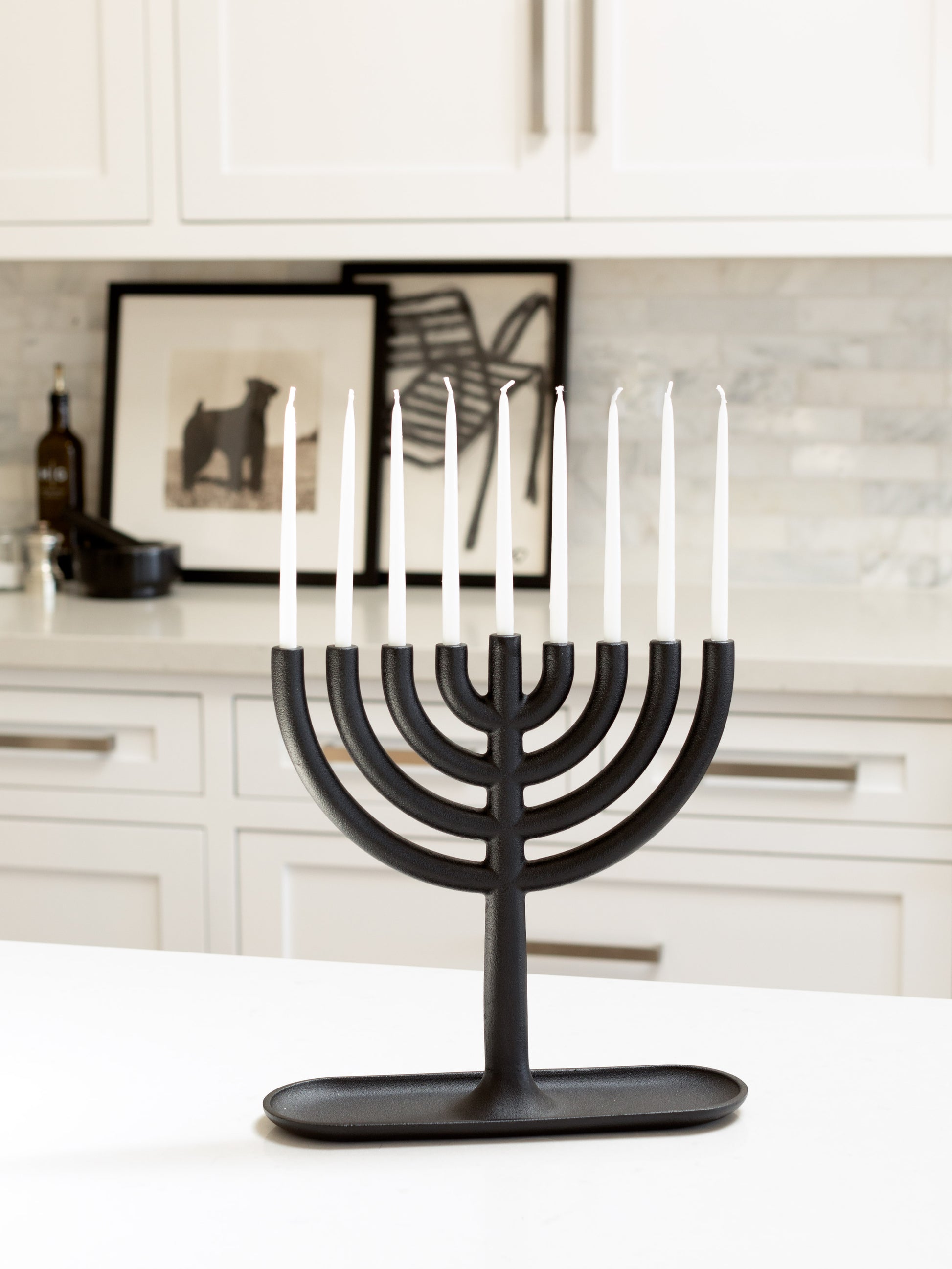Black cast-iron Menorah with eight white, delicate taper candles on a white kitchen counter.