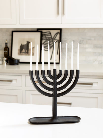 Black cast-iron Menorah with eight white, delicate taper candles on a white kitchen counter.