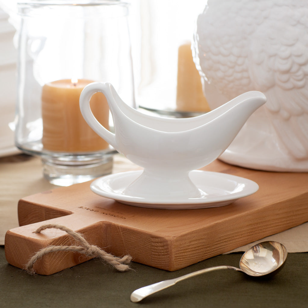 White ceramic Toscana sauce boat with integrated handle and attached oval plate, on a wooden board.