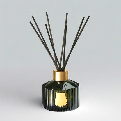 Trudon Abd El Kader reed diffuser in a fluted dark green glass bottle with a gold seal and black rattan sticks.