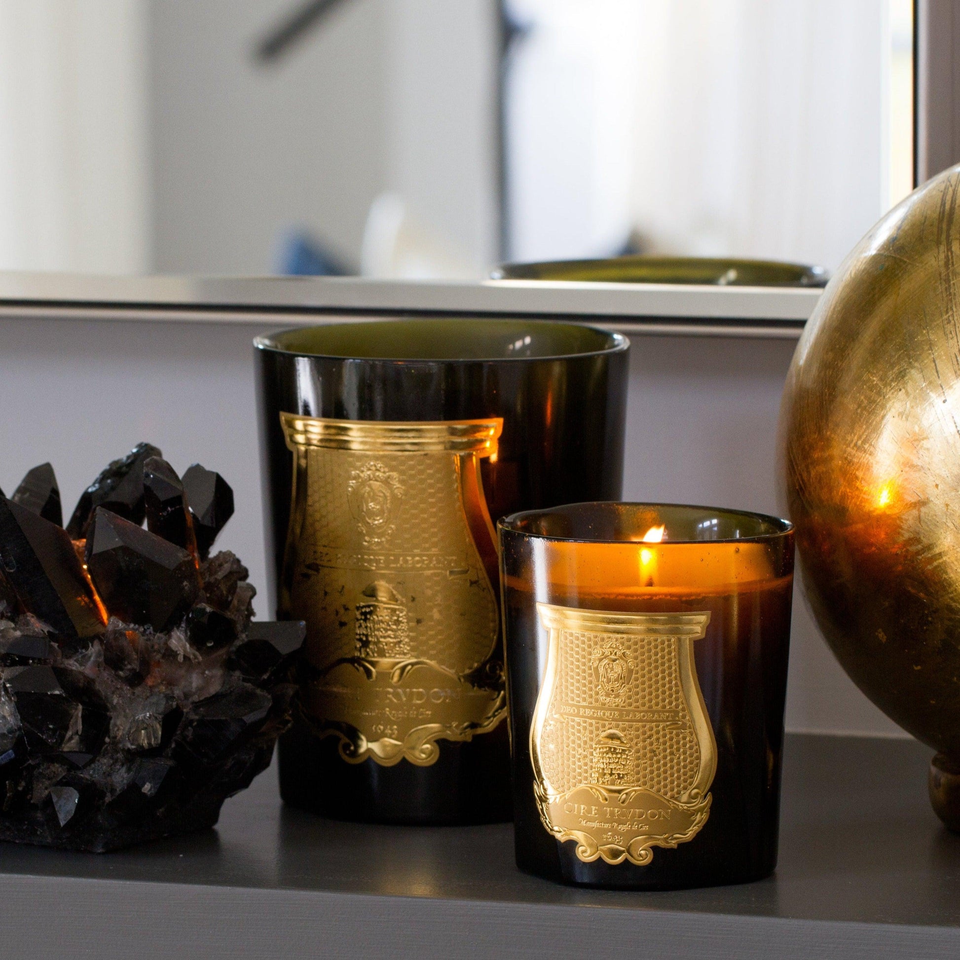 Trudon Solis Rex Classic Scented Candle in a dark green glass vessel with a gold label, next to a smaller lit candle.