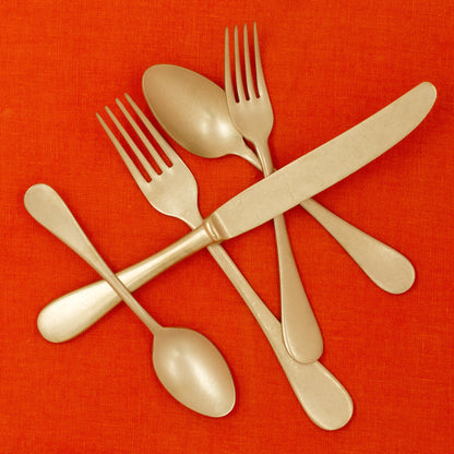 Vintage Oro 5-piece gold-finish stainless steel flatware set on an orange linen background.