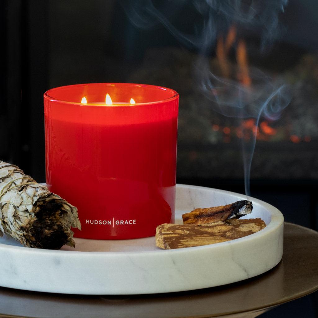 White California sage smudge stick, red candle, and wood incense on a marble tray.