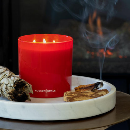 White California sage smudge stick, red candle, and wood incense on a marble tray.