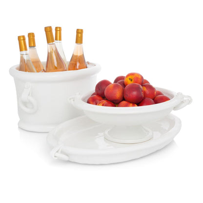 White ceramic oval ice bucket with ring handles, holding rosé wine, next to a matching fruit bowl with peaches.