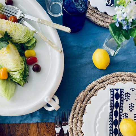 White ceramic oval platter with ring handles, holding a salad, on a blue tablecloth.